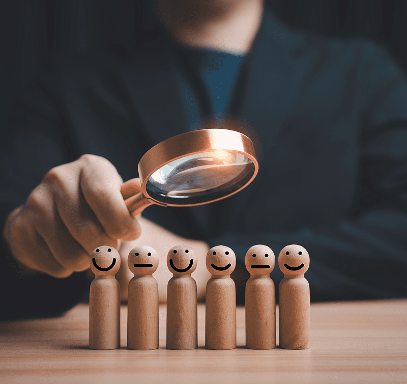Magnifying glass over wooden figures with smiles.