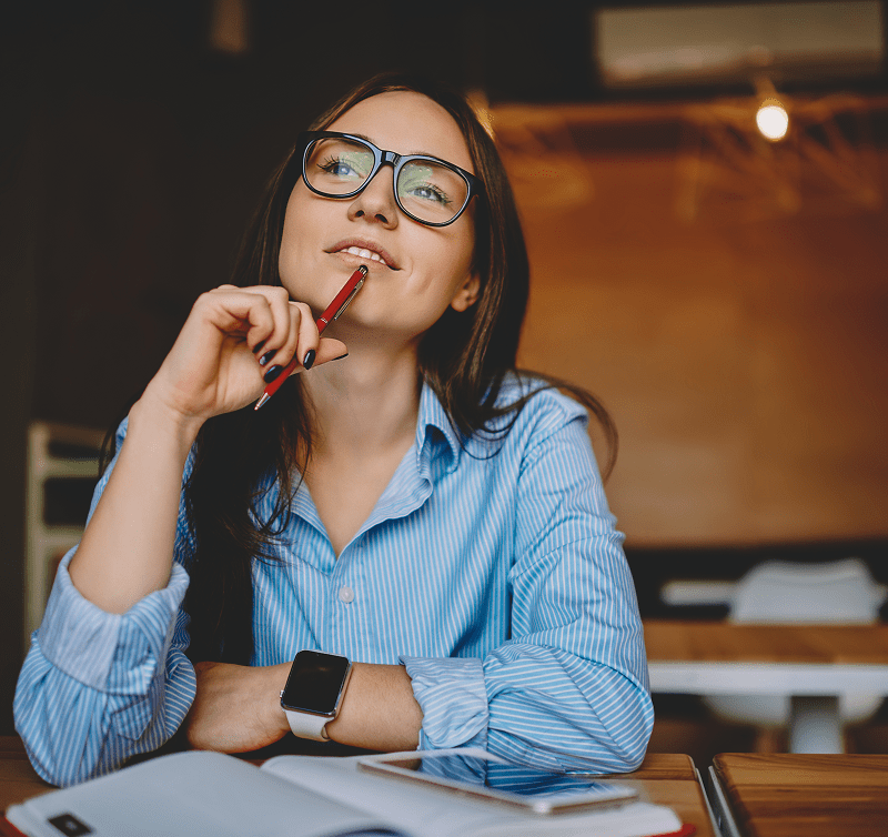 Woman thinking, holding pen in classroom.